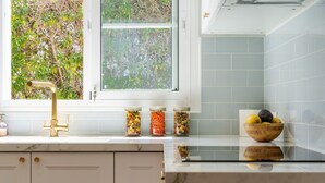 A kitchen with a window, a sink with a gold faucet, and three jars of preserved food on the counter.