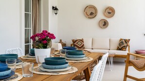 A dining area with a wooden table set with blue plates and bowls, a white vase with pink flowers, and a white sofa with patterned cushions in the background.