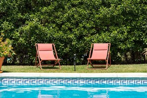 A swimming pool with two lounge chairs and a hedge in the background.