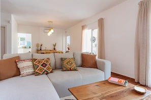 A living room with a sofa, coffee table, and a dining area in the background.