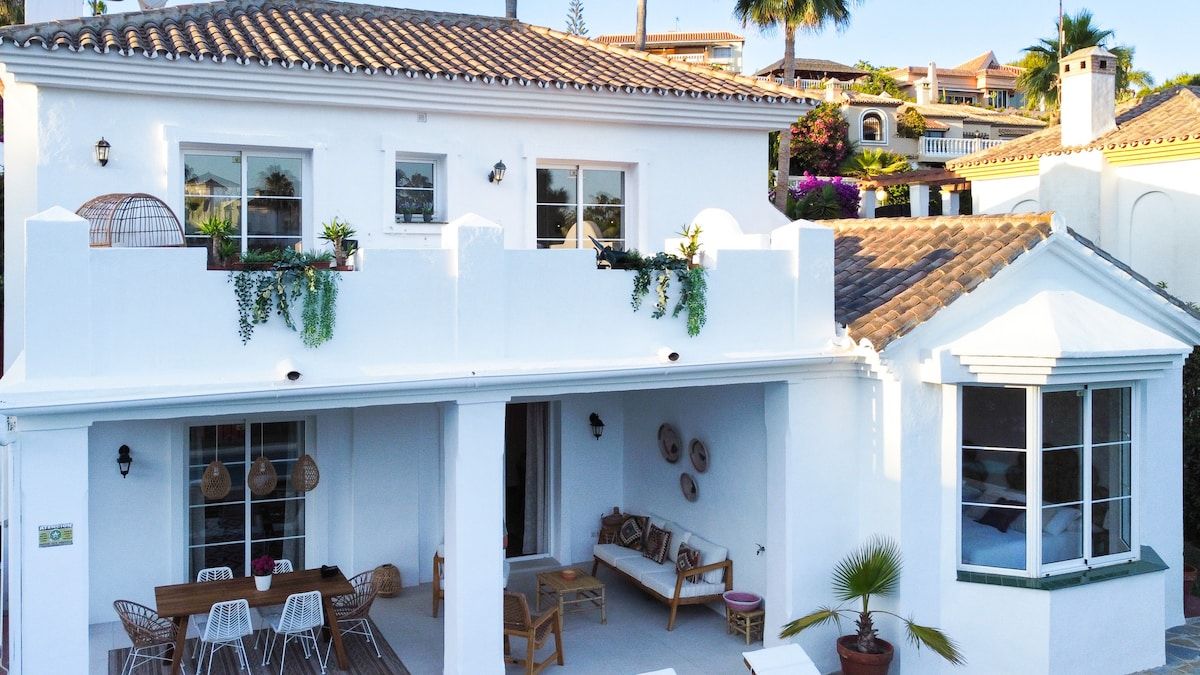 Un bâtiment blanc doté d’un balcon, d’un coin repas et d’un espace détente avec des coussins.