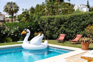 A swimming pool with a swan float, surrounded by greenery and red lounge chairs.