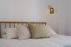 Una cama con cabecera de madera, una lámpara fijada a la pared y dos almohadas.