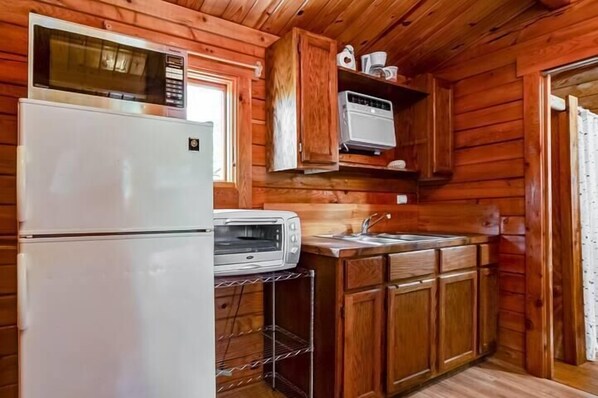 Una cocina con paredes de madera, un refrigerador, un microondas, un tostador y un lavamanos.