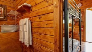 Interno di una baita in legno con letti a castello, un lampadario, uno scaffale con un cesto e un quadro appeso al muro.