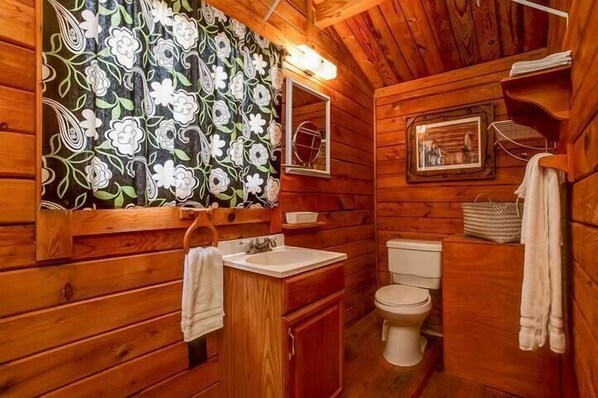 Un baño de cabaña de madera con lavabo, inodoro y espejo.