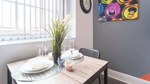 A dining area with a table set for two, a potted plant, and a colorful abstract painting on the wall.