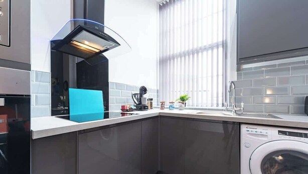 Une cuisine moderne équipée d’un lave-vaisselle encastré, d’une cuisinière et d’une fen être avec des stores.