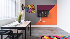 Un coin repas avec une table dressée pour deux personnes, une plante en pot et un téléviseur fixé au mur.