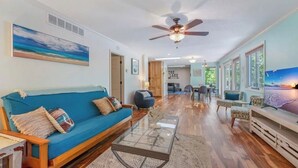 A spacious living room with a blue sofa, a glass coffee table, and a ceiling fan. There is a dining area with a table and chairs in the background. - Quiet Lakefront - Hot Tub! H2O Toys! Pet Friendly! (Linn Creek)