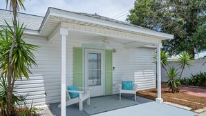 A white house with a covered porch, two white chairs with blue cushions, and green shutters.