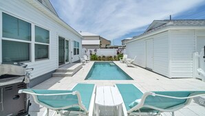 A backyard with a swimming pool, two lounge chairs, a barbecue grill, and a covered patio area.