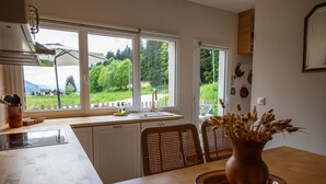 Eine Küche mit einem großen Fenster, einem Esstisch mit Stühlen und einer Vase mit getrockneten Blumen.