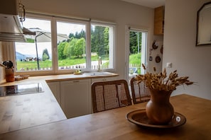A kitchen with a large window, a dining table with chairs, and a vase of dried plants on the table.