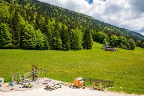 A playground with a slide, swings, and a small wooden structure, set against a backdrop of a forested hillside. - New renovated studio heart of the Vercors (Autrans-Méaudre en Vercors)