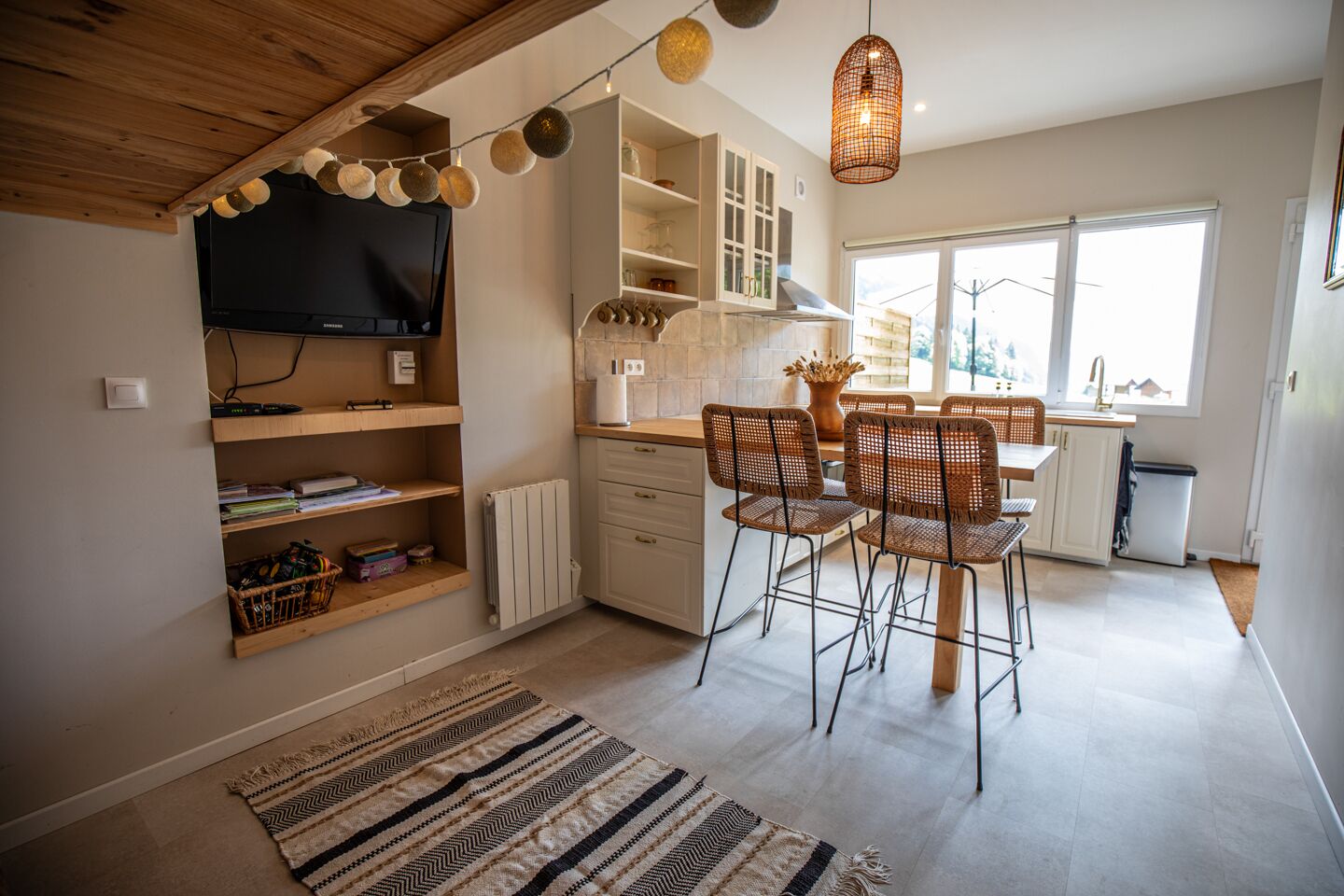 Une cuisine moderne avec un coin repas, un plafond en bois et un téléviseur fixé au mur.