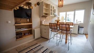 Une cuisine moderne avec un coin repas, un plafond en bois et un téléviseur fixé au mur.