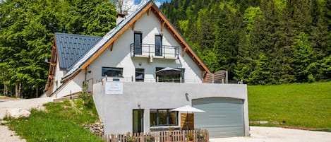Un chalet à deux étages, doté d’un toit en pente, d’un balcon et d’un garage.