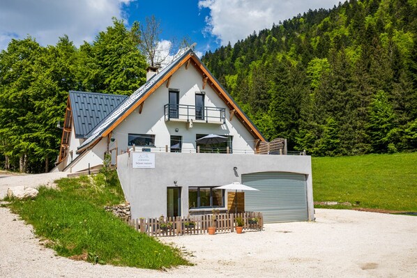 Un chalet à deux étages, doté d’un toit en pente, d’un balcon et d’un garage.