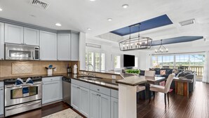 A modern kitchen with built-in appliances, a dining area with a large island, and a view of the outdoors.