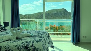 Ein Schlafzimmer mit Bett, Blick auf einen Berg und einem Balkon mit blauen Vorhängen.
