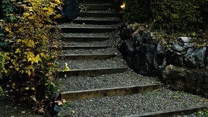 A set of stone steps leading up to a wooden deck, surrounded by dense foliage and a wooden fence. - Points West Oceanfront Rooftop suite (Sooke)