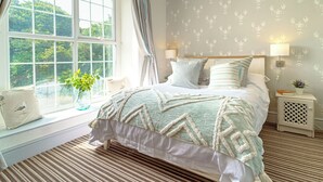 A bedroom with a large window, a bed with striped pillows, a bedside table with a lamp, and a wall with a lobster pattern. - This family home is situated in the gorgeous village of Bull Bay on Anglesey. (Bull Bay)