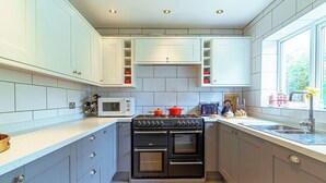 A compact kitchen with white cabinets, a built-in microwave, a gas stove, and a double oven. - This family home is situated in the gorgeous village of Bull Bay on Anglesey. (Bull Bay)