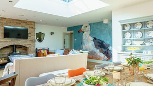 A dining area with a high ceiling, a fireplace, and a wall mural. - This family home is situated in the gorgeous village of Bull Bay on Anglesey. (Bull Bay)