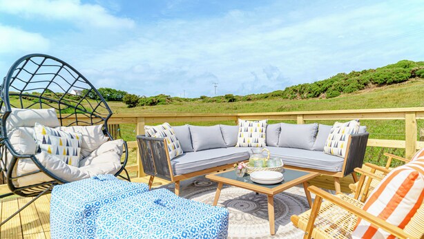 A deck with outdoor furniture, including a sofa, chairs, and a hanging chair. - This family home is situated in the gorgeous village of Bull Bay on Anglesey. (Bull Bay)