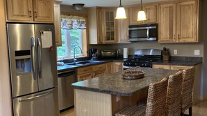 Une cuisine moderne avec des meubles en bois, des appareils en acier inoxydable, un îlot central doté de tabourets de bar et un éclairage suspendu.