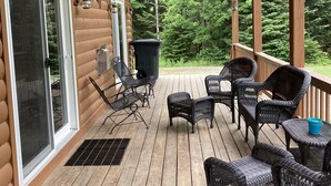 Une terrasse en bois, meublée de meubles en osier, avec vue sur une forêt.