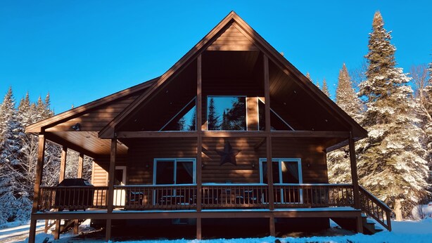 Une cabane en bois dotée d’un balcon, entourée d’arbres couverts de neige.