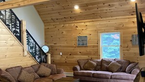 L’intérieur d’un chalet accueillant, avec des murs en bois, un escalier en bois, deux canapés, une table basse et un tapis à motifs.