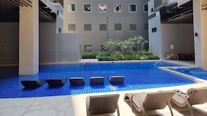 A modern building with a pool area, including lounge chairs and a small garden. - Mel and Rose Place at S Residences Tower 1 Mall of Asia Area (Pasay)