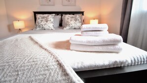 Un letto rifatto con una coperta bianca e cuscini, una pila di asciugamani piegati e due abat-jour.
