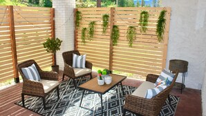 Patio esterno con mobili in vimini, un tavolo e piante pensili.