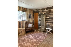 Una habitación rústica con paredes de madera, un sillón de cuero, un tapete estampado y un radiador grande.