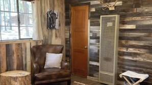A rustic room with wooden walls, a leather chair, a patterned rug, and a large heater.