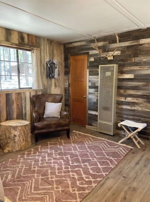 Une pièce rustique aux murs en bois, avec un fauteuil en cuir, un tapis à motifs et un grand radiateur.