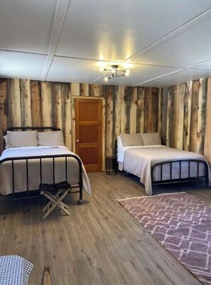 Una habitación con dos camas, paredes de madera, una lámpara en el techo y suelo de madera.