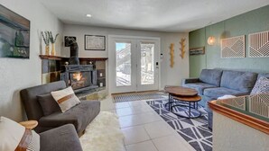 Ein gemütliches Wohnzimmer mit Kamin, einer grauen Couch, einem Couchtisch und einem gemusterten Teppich.