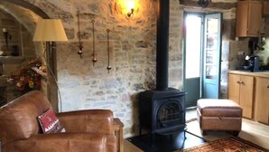 A cozy living room with a stone wall, a black wood-burning stove, a leather sofa, and a wooden cabinet. - La Salesse, Restored farmhouse in idyllic rural location + private pool (Ginals)
