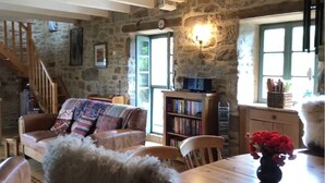 A rustic stone interior with a wooden staircase, a sofa with a colorful blanket, a bookshelf, and a dining table with a vase of flowers. - La Salesse, Restored farmhouse in idyllic rural location + private pool (Ginals)