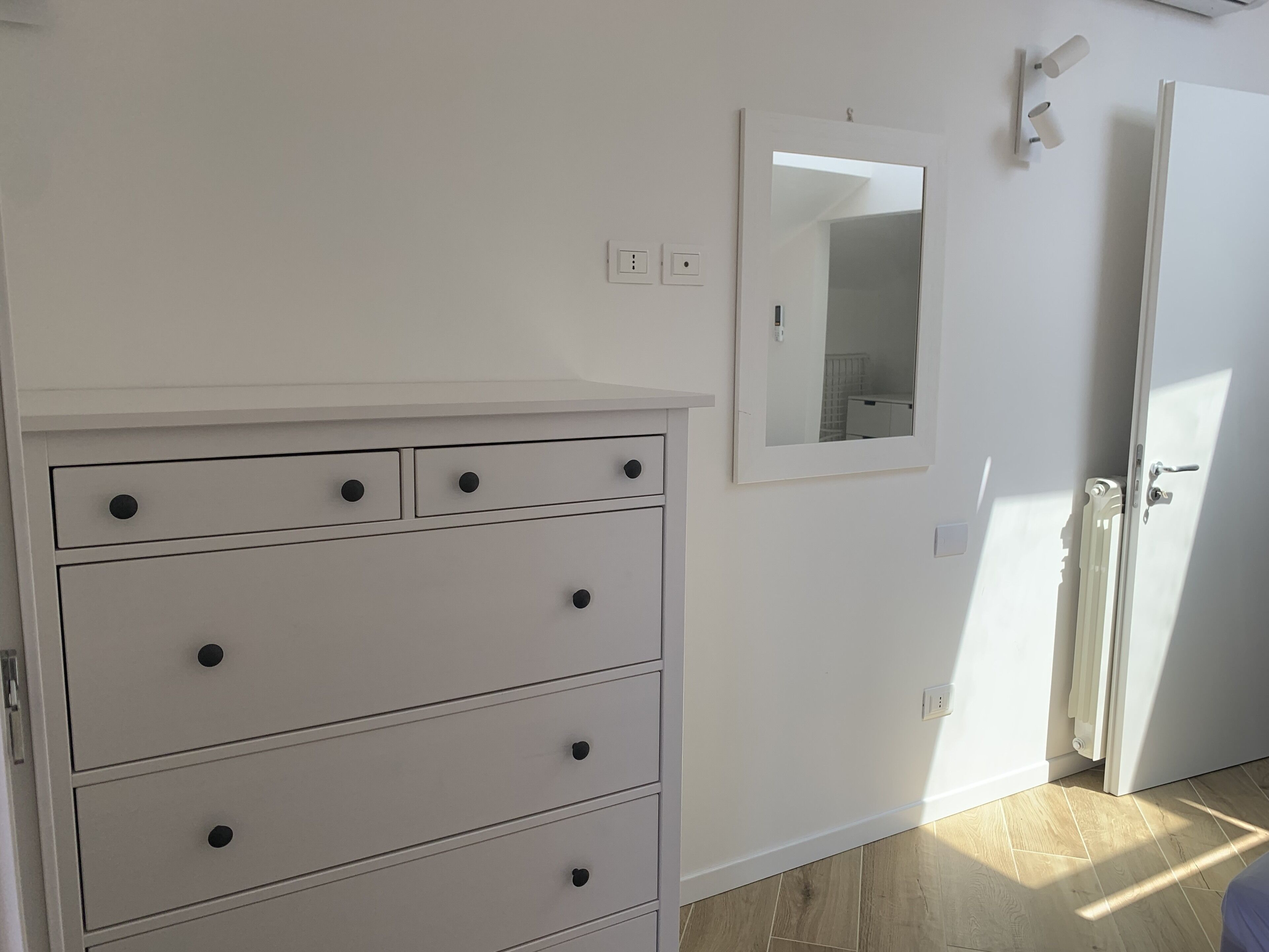 Una habitación con un aparador blanco, un espejo y una puerta.
