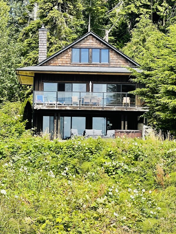 A two-story house with a balcony, surrounded by lush greenery.