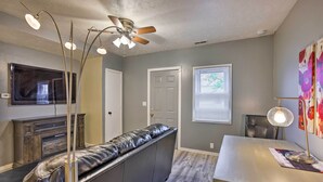 Un salon moderne avec un banc en cuir, un ventilateur de plafond, un téléviseur à écran plat et une table à manger avec une lampe.