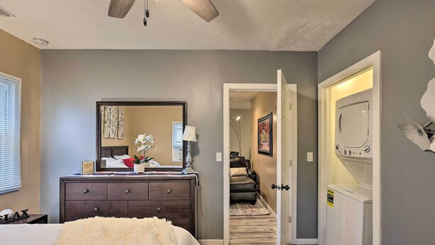 Une chambre à coucher comprenant un lit, une commode, un miroir et une porte donnant sur une buanderie.