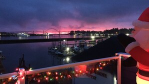 Vista nocturna de un puerto deportivo con barcos, un puente y luces festivas.