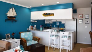 Una cocina compacta con un refrigerador blanco, taburetes de bar blancos y una pared azul decorada con motivos náuticos.